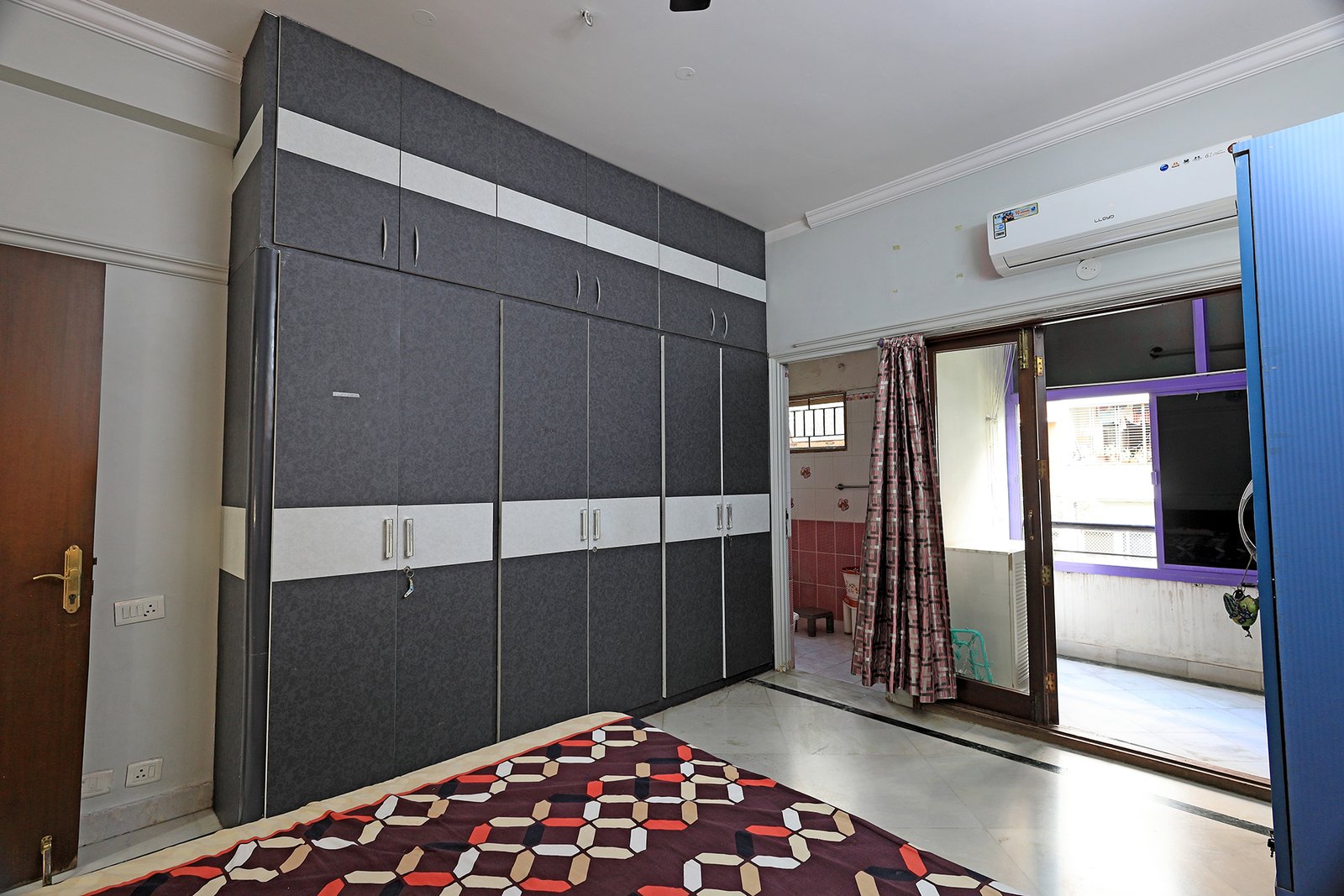Bedroom 2 with floor-to-ceiling wooden wardrobe and overhead storage, with the attached bathroom beyond